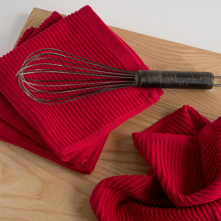 Red ribbed kitchen towels with a metal whisk on a wooden surface