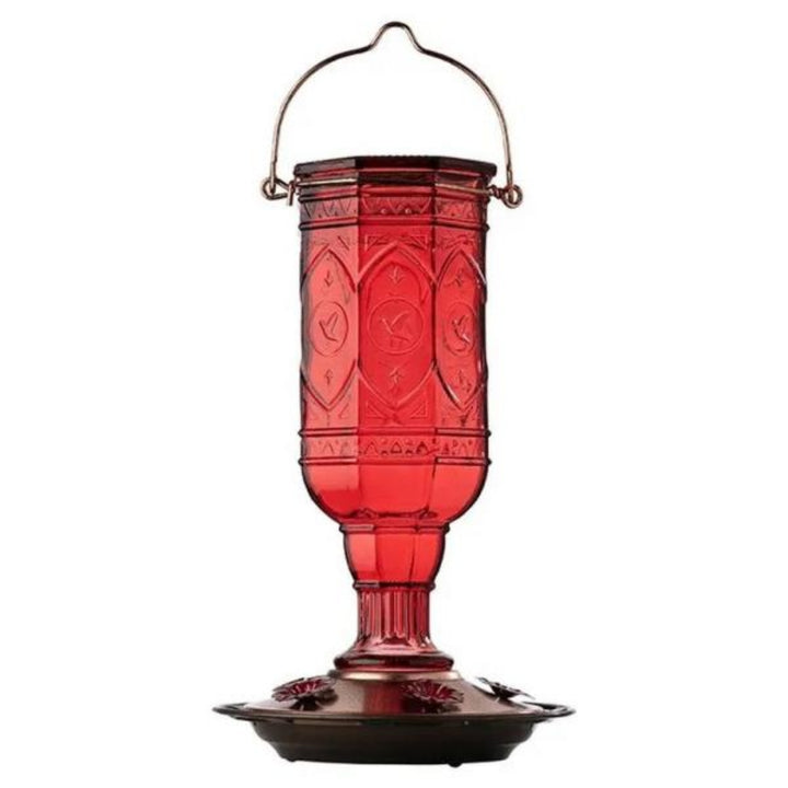 Red glass hummingbird feeder with decorative patterns on a white background