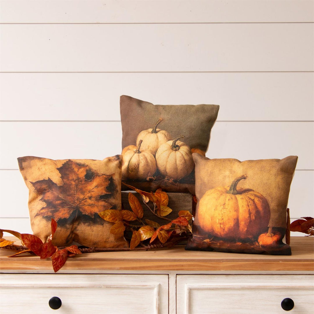 Decorative pillows with pumpkin and leaf patterns on a wooden surface.