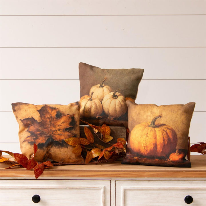 Decorative pillows with pumpkin and leaf patterns on a wooden surface.