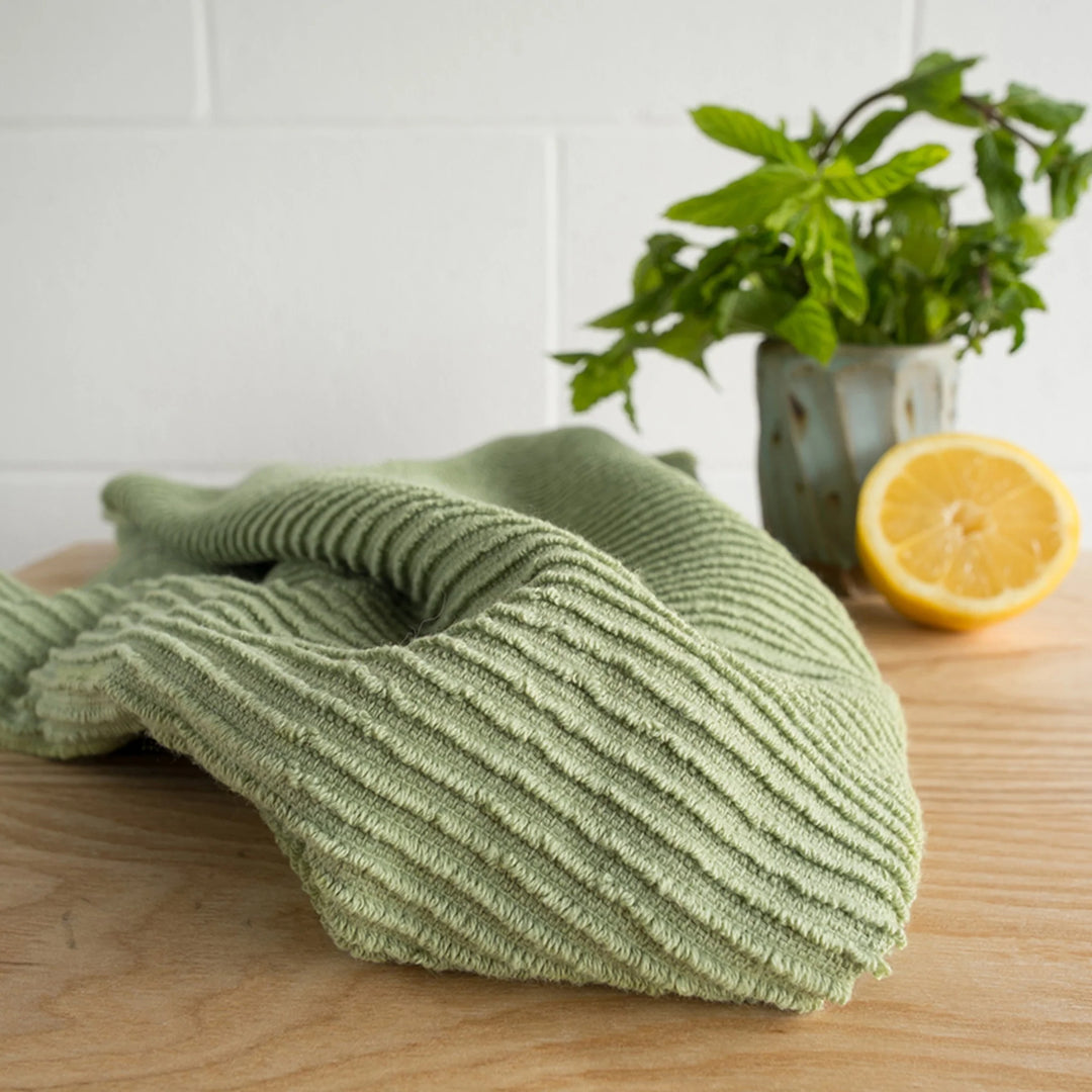 Green microfiber cloth on a wooden surface with a lemon and plant in the background