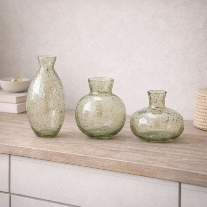 Three green glass vases on a wooden surface with a neutral background