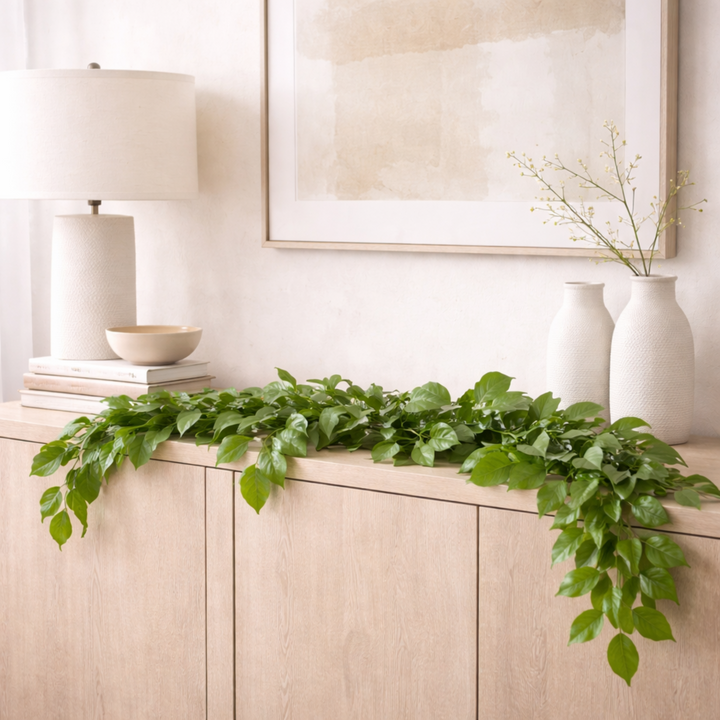 Decorative mantel with green leaves, a lamp, and framed artwork.