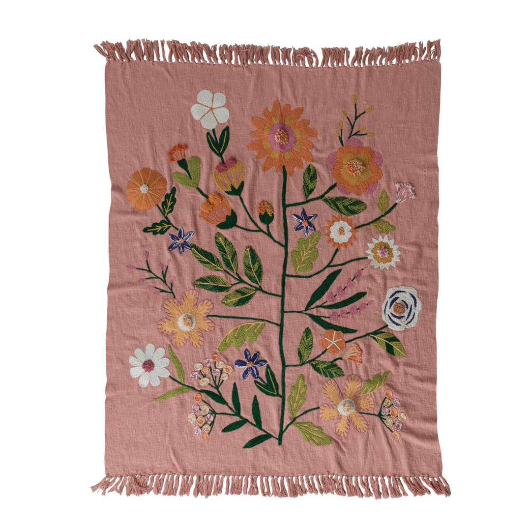 Pink woven blanket with floral patterns and fringes on a white background