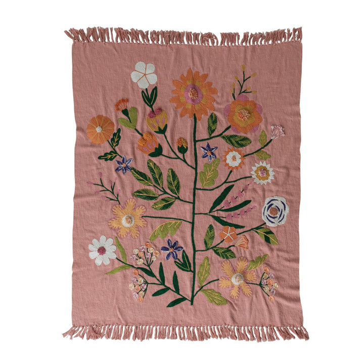 Pink woven blanket with floral patterns and fringes on a white background