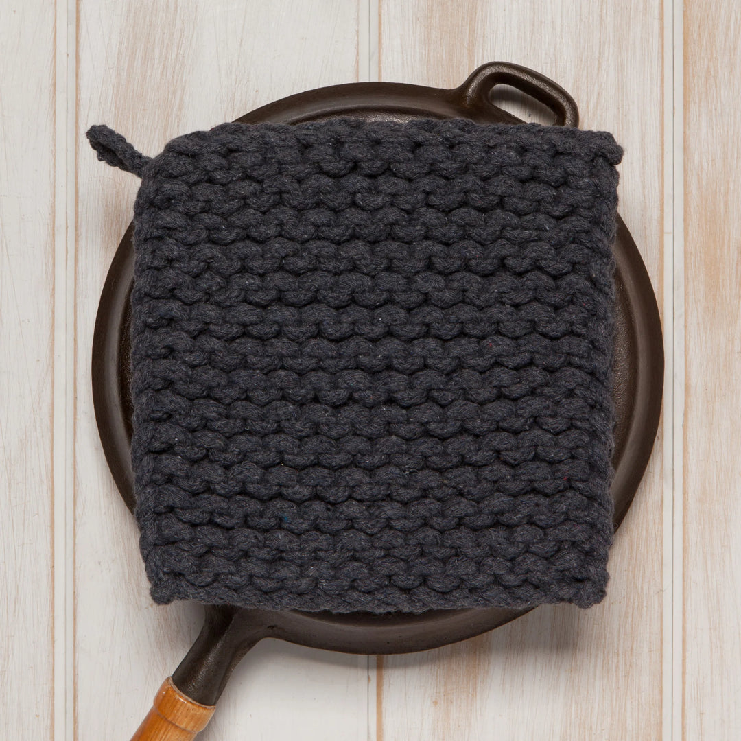 Dark gray knitted potholder on a cast iron skillet against a wooden background