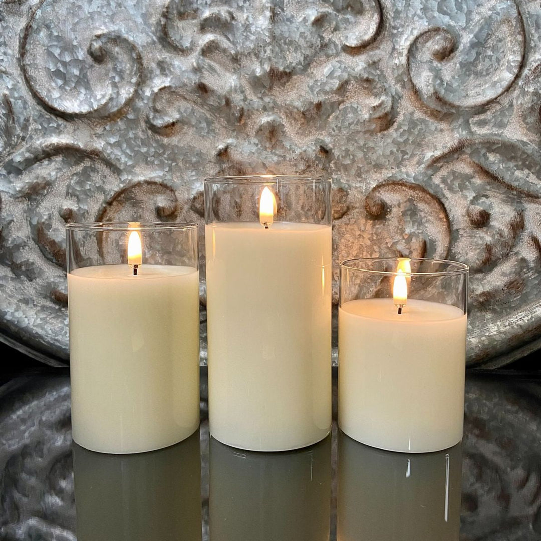 Three lit candles in glass holders against a decorative metallic wall.