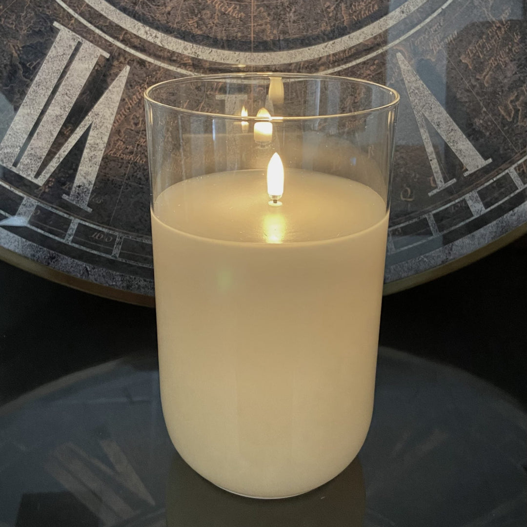 Candle in a glass holder with a clock in the background