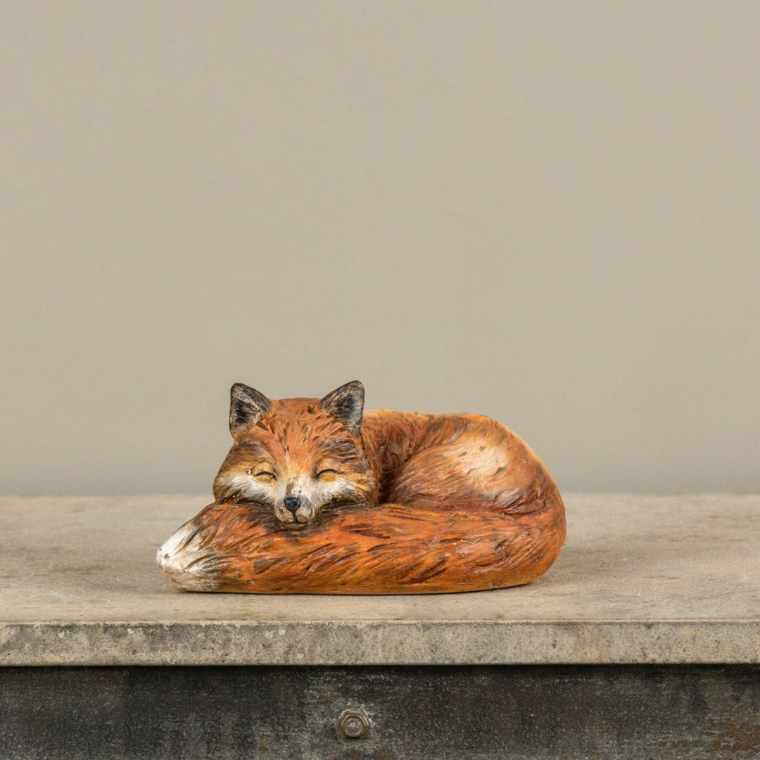 Sleeping fox figurine on a wooden surface with a neutral background