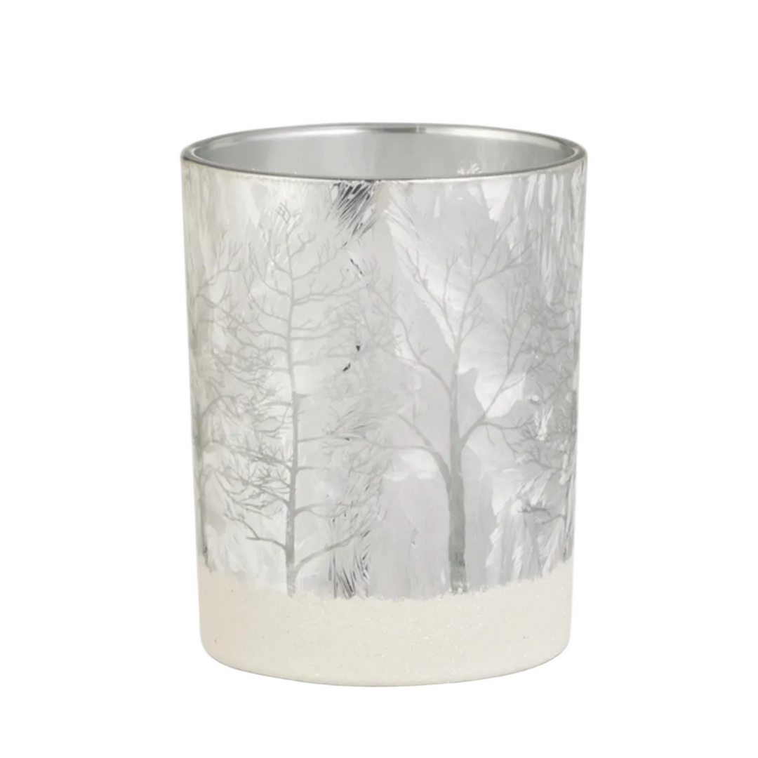 A cylindrical metal candle holder or tumbler with a frosted winter forest design, featuring bare tree silhouettes on a silver background with a textured off-white base.