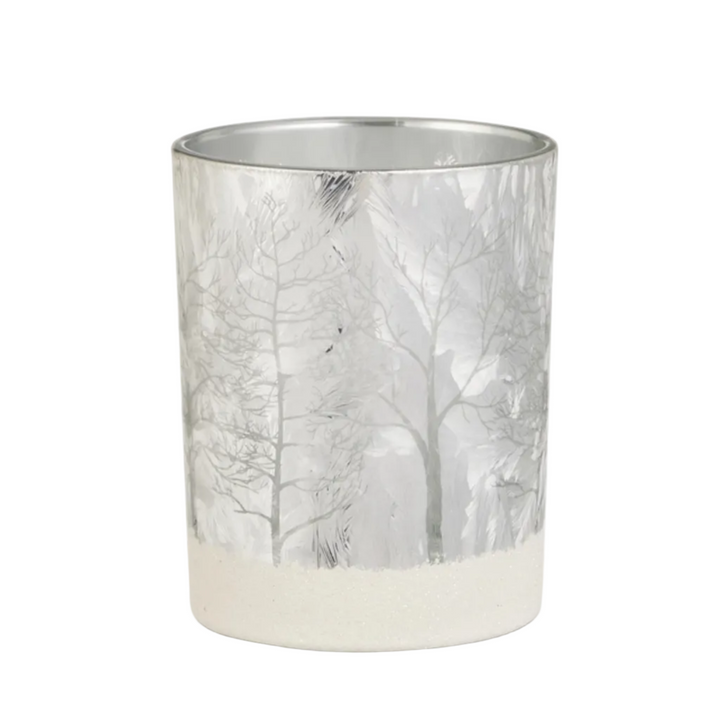 A cylindrical metal candle holder or tumbler with a frosted winter forest design, featuring bare tree silhouettes on a silver background with a textured off-white base.