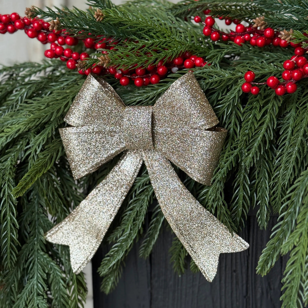 Decorative Christmas garland with a silver bow and red berries on a wooden surface.