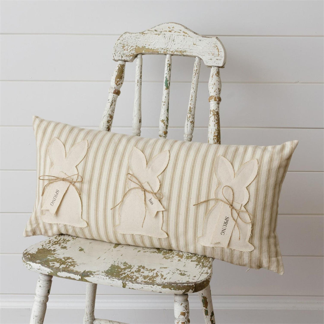 Decorative pillow with bunny designs on a rustic chair against a wooden wall.