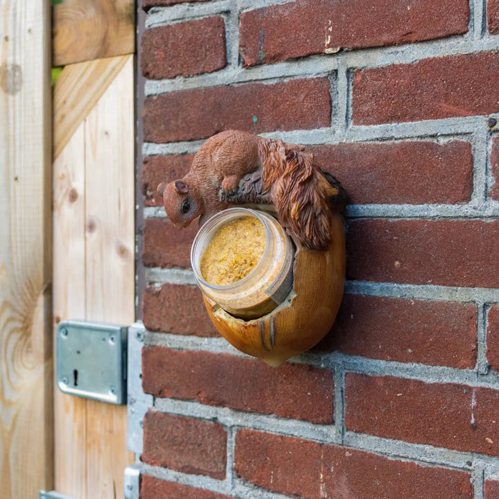 Squirrel climbing a brick wall next to a jar of sunflower seeds