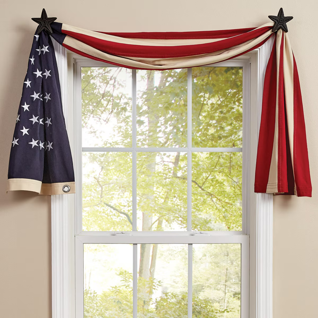 Decorative American flag hanging above a window with a view of trees.