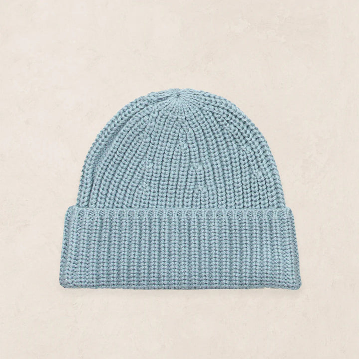 A light blue knit beanie hat with a ribbed cuff, displayed flat against a light beige textured background.