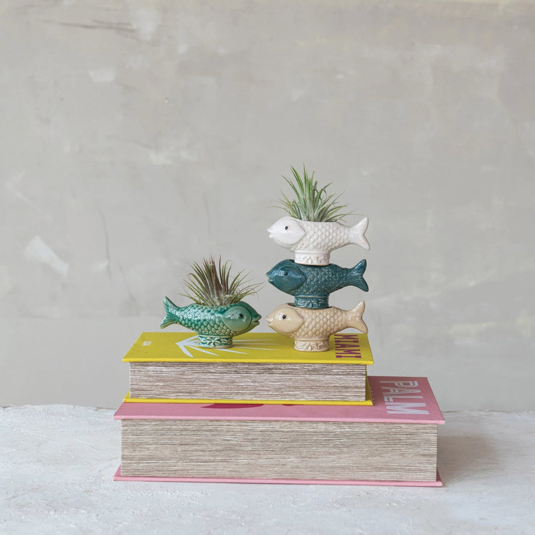 Decorative fish-shaped planters with air plants on a stack of books against a neutral background