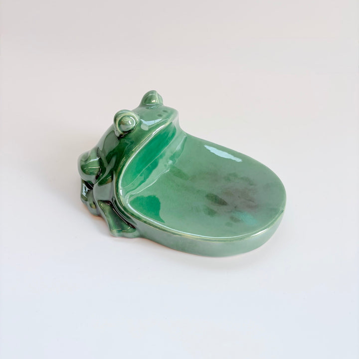 A glossy green ceramic frog-shaped dish, resembling a tree frog, with a smooth rounded bowl and raised legs, photographed on a clean white background.