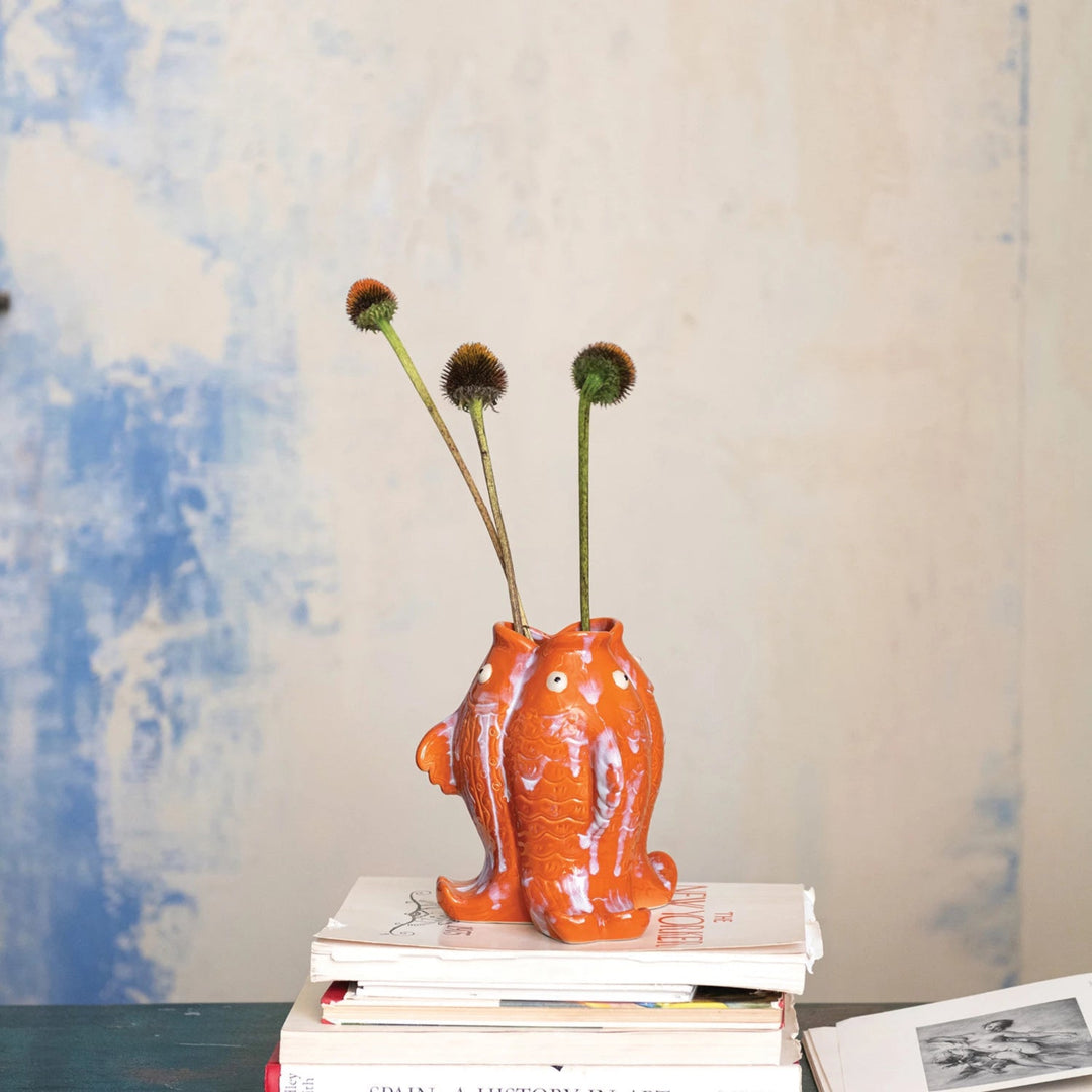 Orange cat-shaped vase with dried plants on a stack of books against a blue and white abstract background