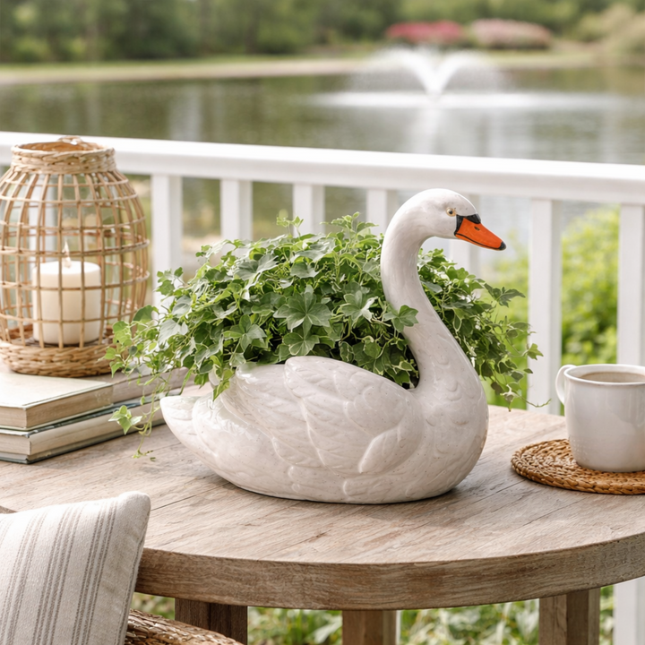 White swan-shaped planter with greenery on a wooden table by a lake.