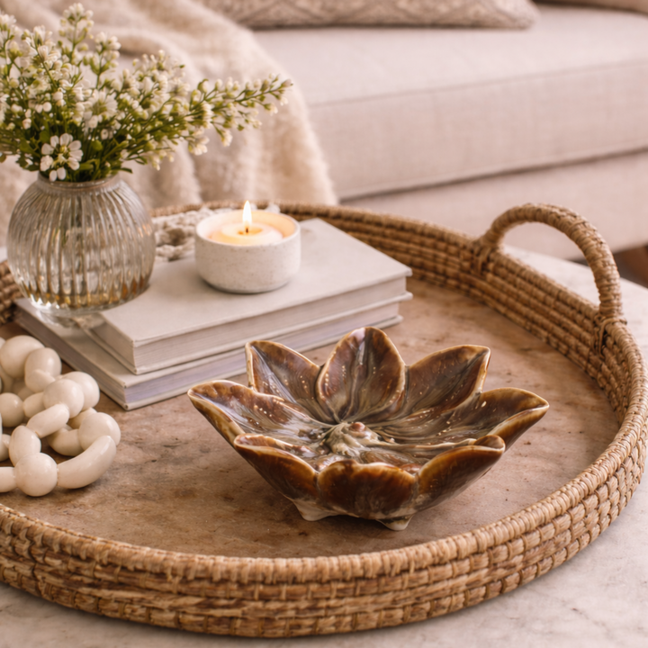 Decorative tray with a ceramic bowl, candle, and flowers on a coffee table.