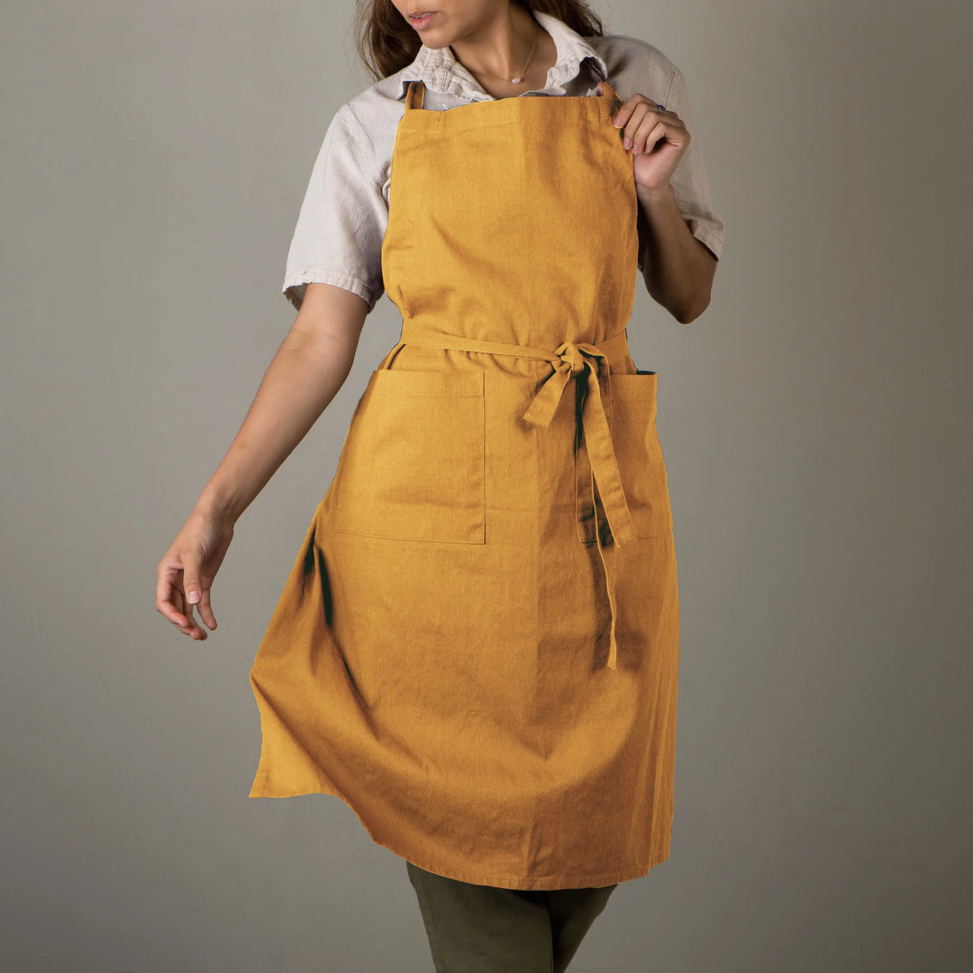 Person wearing a mustard yellow apron against a gray background