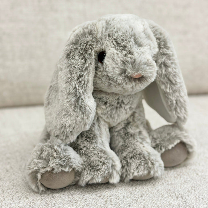 A plush gray bunny with a soft texture, floppy ears, and a pink flocked nose. The bunny has a fluffy tail and is sitting upright on a soft surface.