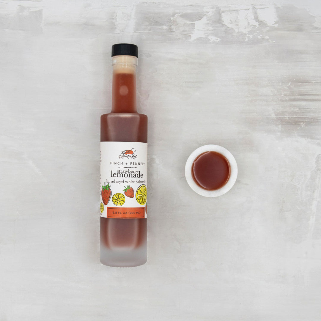 Bottle of strawberry lemonade with a small bowl of liquid on a textured white surface