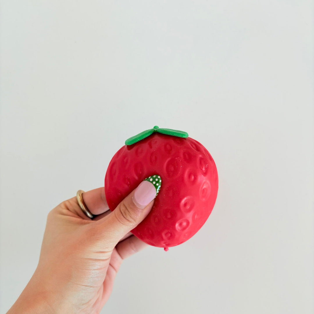 Hand holding a red strawberry-shaped object against a light gray background