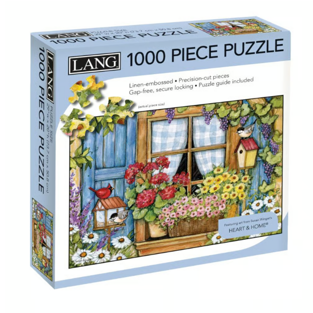 A boxed 1000-piece jigsaw puzzle by Lang, featuring a colorful illustration of a garden window with flowers, a birdhouse, curtains, and a red bird. The box is shown at a slight angle against a plain white background.