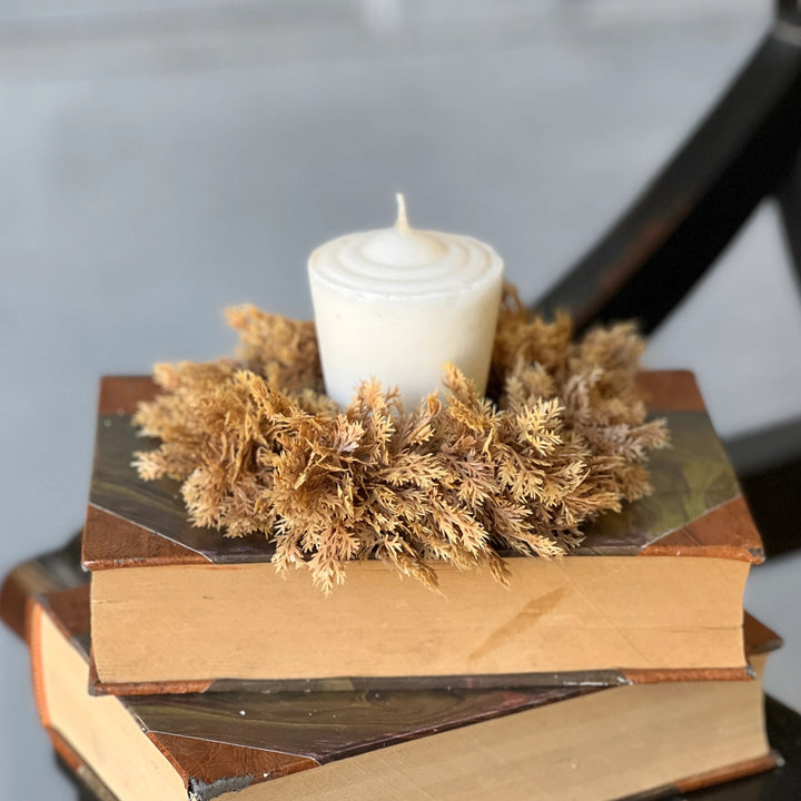 Stack of books with a candle and decorative grass on top, placed on a surface.