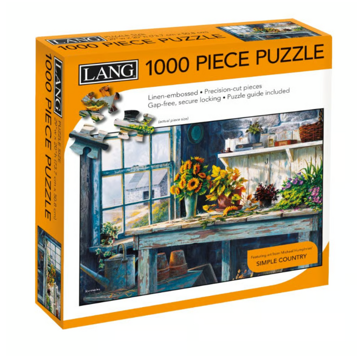 A Lang 1000-piece jigsaw puzzle box titled 'Simple Country'. The packaging features a vibrant orange border and a detailed illustration of a rustic country kitchen scene with a weathered wooden table, shelves, and a window with sunflowers.