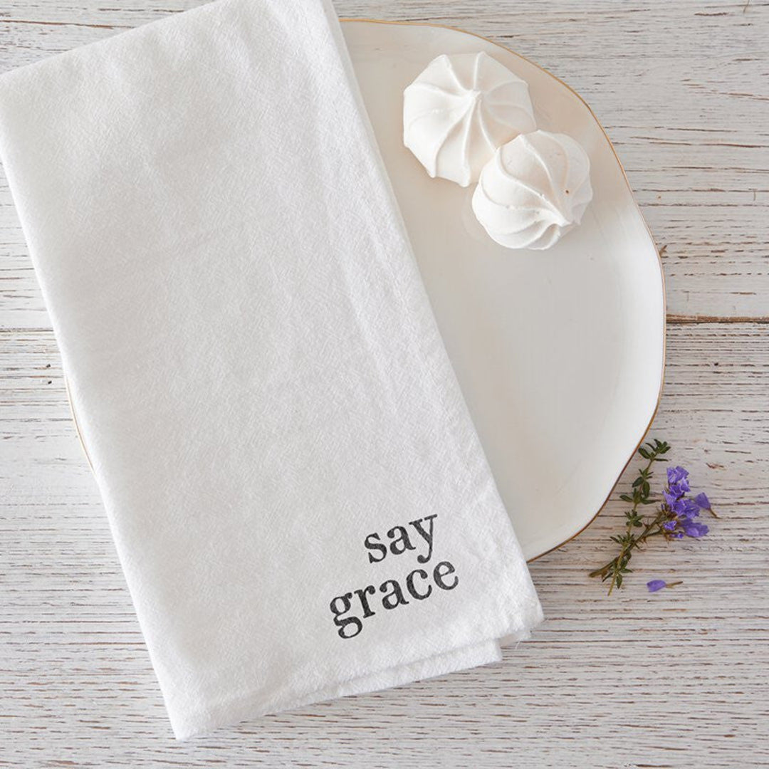 White towel with 'say grace' text on a wooden surface with flowers.