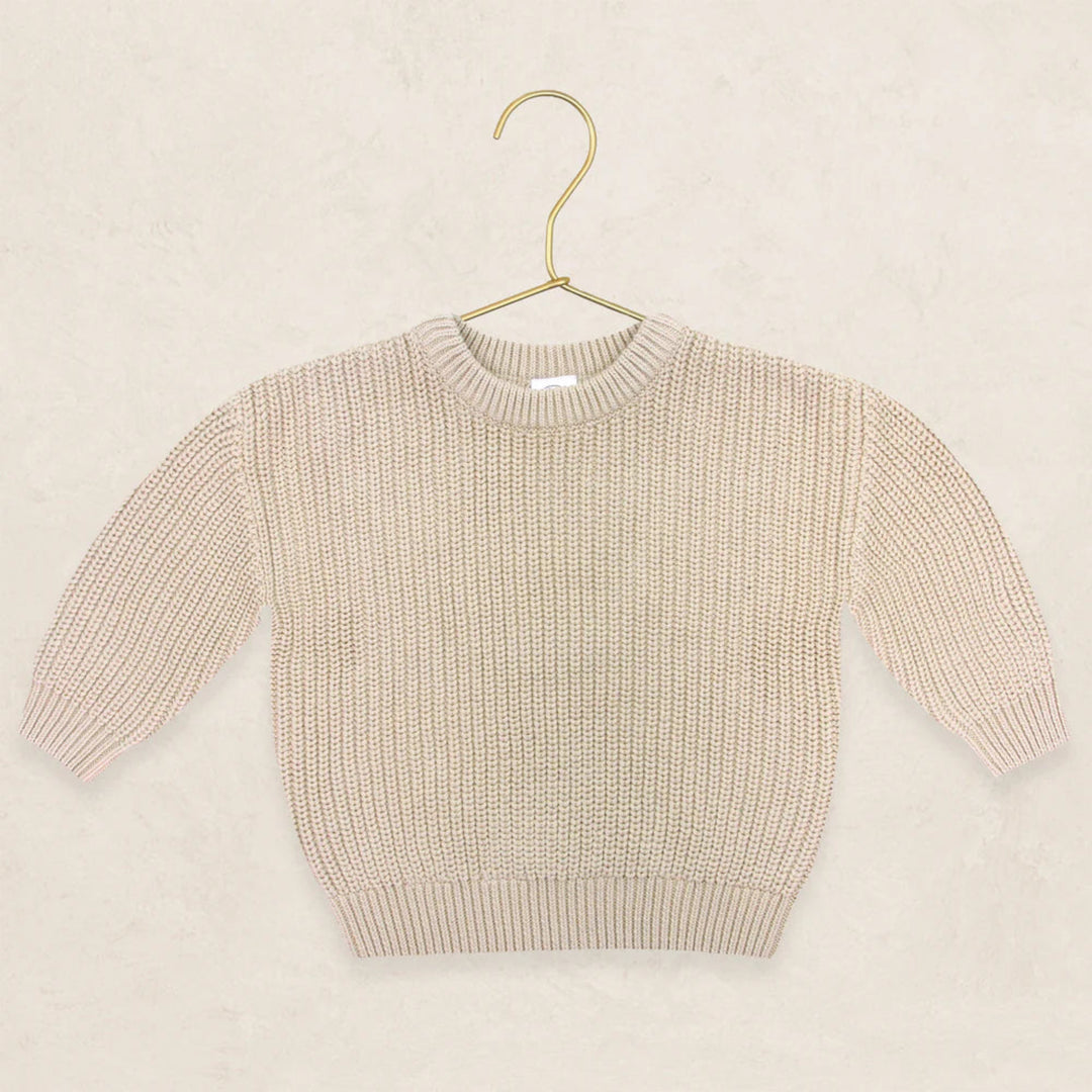 A cream-colored ribbed knit long-sleeve sweater displayed on a gold metal hanger against a textured beige background.