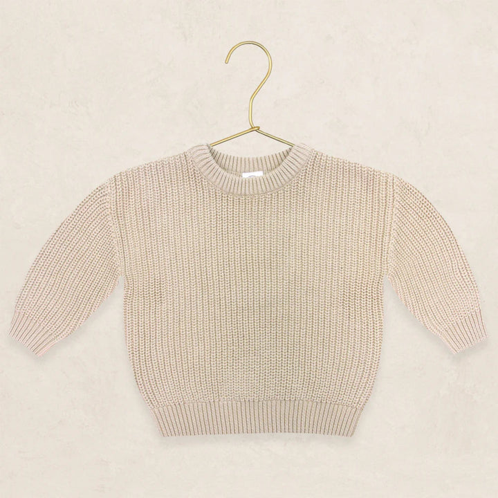 A cream-colored ribbed knit long-sleeve sweater displayed on a gold metal hanger against a textured beige background.