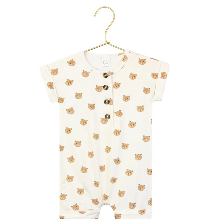 A baby short-sleeve romper in off-white with a repeating pattern of small brown bear faces, hanging on a gold hanger against a white background. A circular inset in the bottom-left corner shows a close-up of the bear pattern.