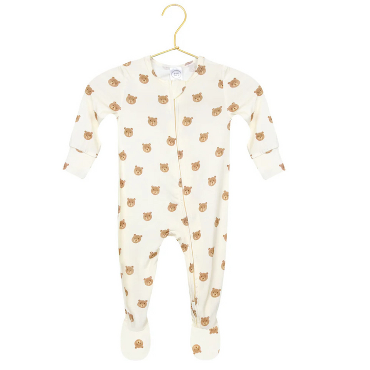 A cream-colored baby footed sleeper with an all-over brown teddy bear face print, hanging on a gold hanger against a white background, with a circular inset showing a close-up of the pattern.