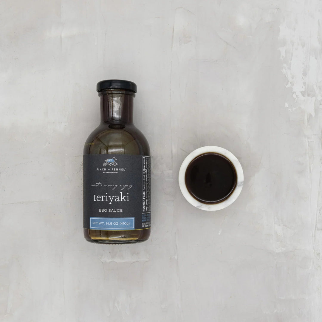 Bottle of teriyaki BBQ sauce with a small bowl of sauce on a light gray background