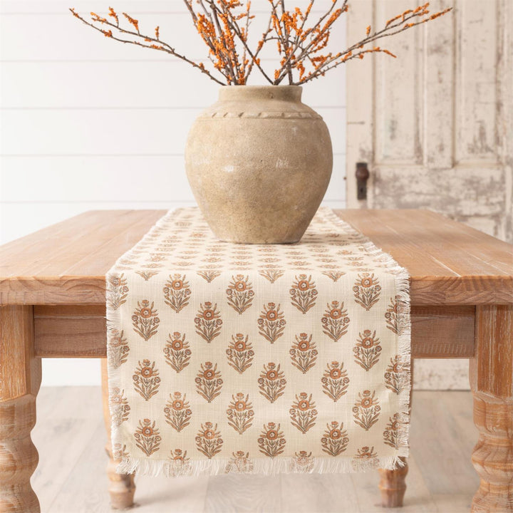 Decorative table runner with floral pattern on a wooden table with a vase and branches.