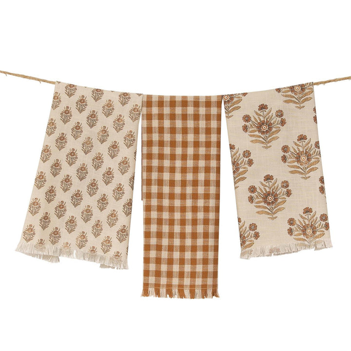 Three scarves with floral and checkered patterns hanging on a line.