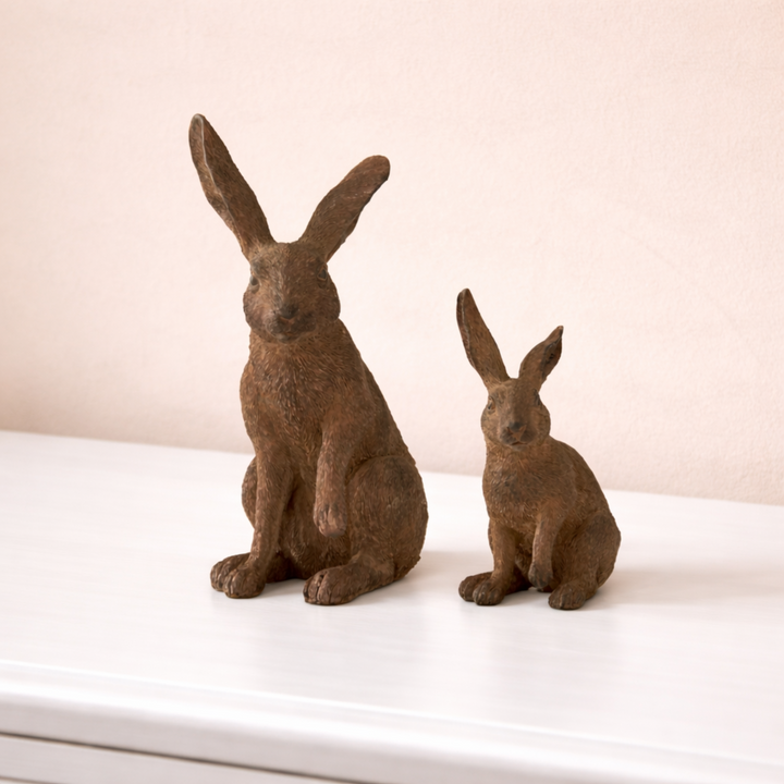 Two brown rabbit statues on a white surface with a beige background