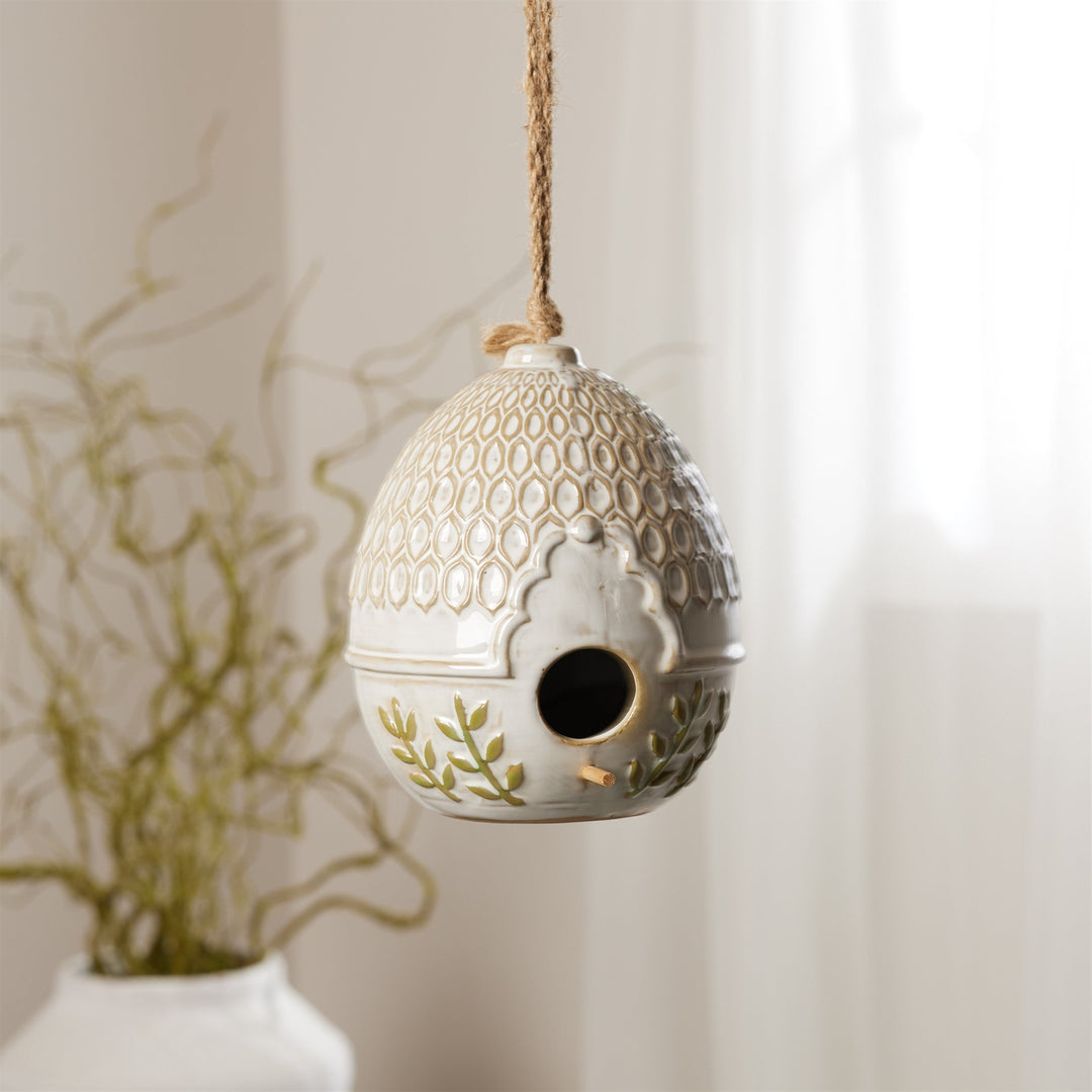 Decorative ceramic birdhouse with intricate patterns hanging against a neutral background.
