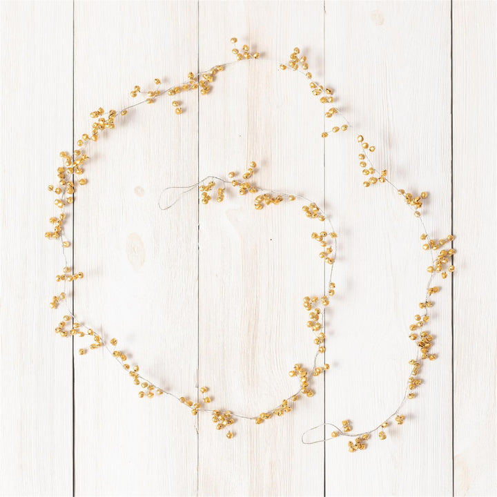 A decorative garland of small golden-yellow berries or dried floral clusters arranged in a loose circle on a white wooden plank background.
