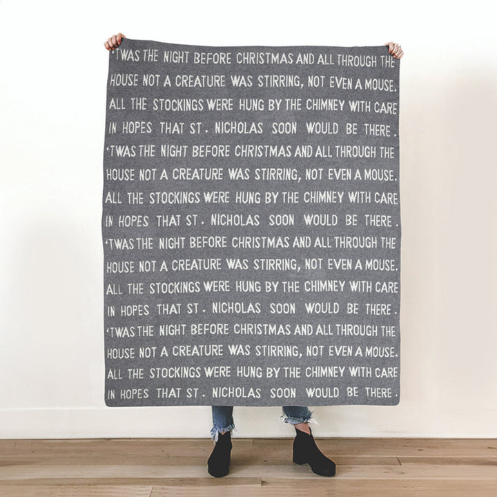 Person holding a blanket with text of 'The Night Before Christmas' against a white wall.