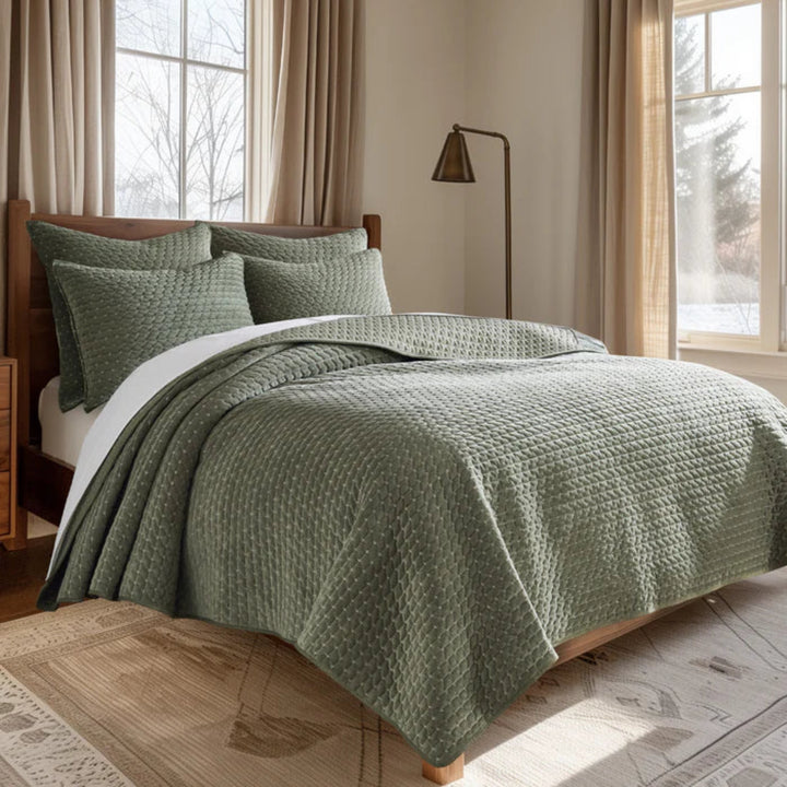 Green quilted bedding set on a bed in a well-lit room with large windows.