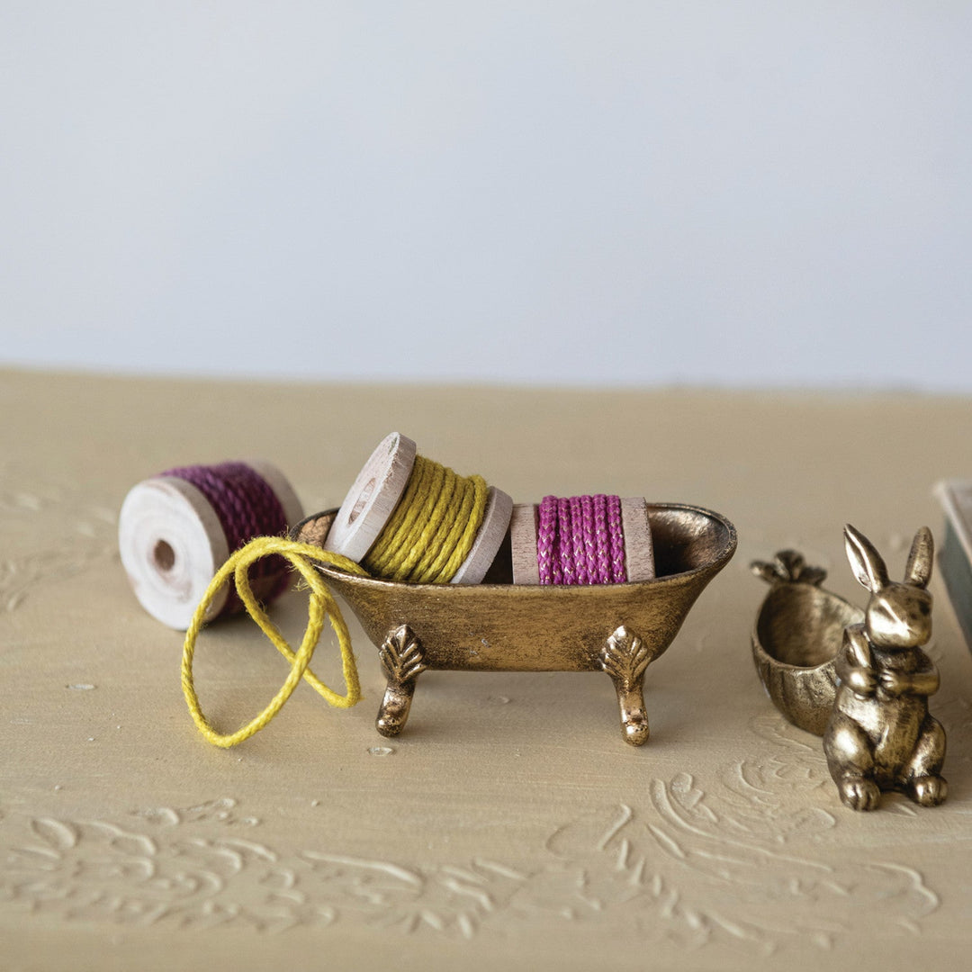 Small wooden bowl with spools of thread and a decorative rabbit figurine on a textured surface.