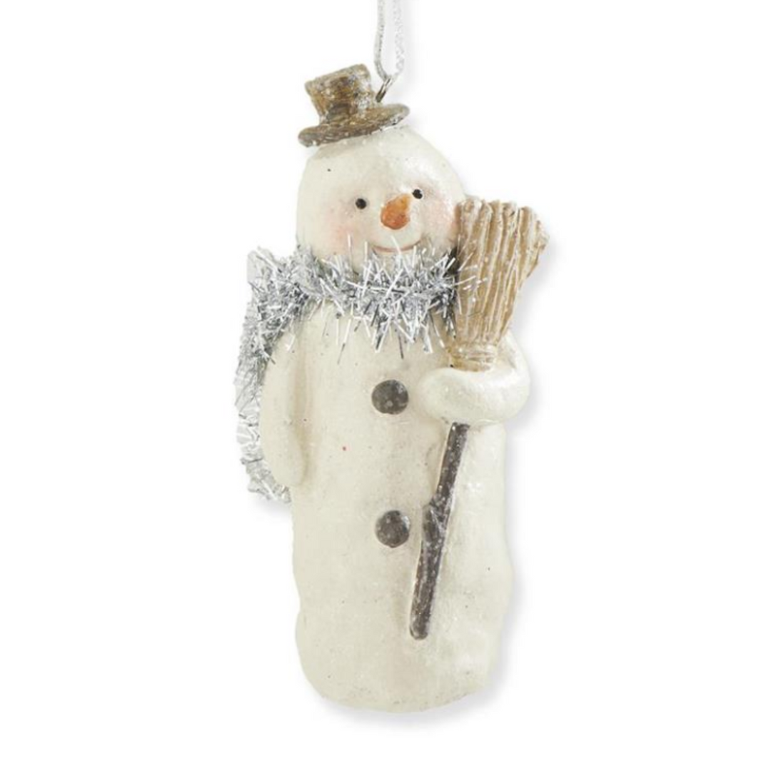 A snowman Christmas ornament in an off-white finish, wearing a brown top hat, a silver tinsel scarf, and holding a brown broom. The ornament is shown against a plain white background.