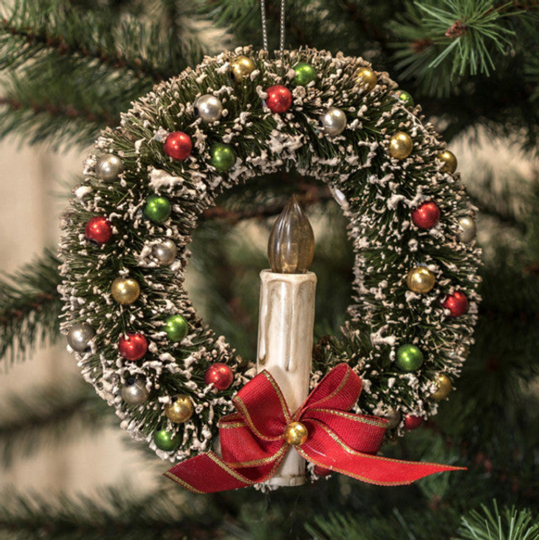 Decorative Christmas wreath ornament with candles and colorful beads on a tree.