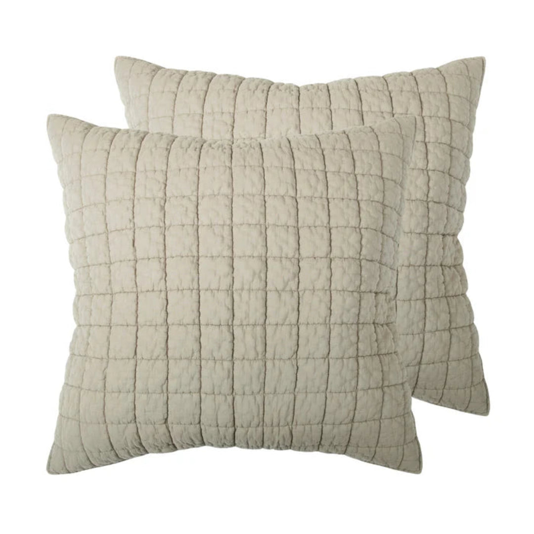 Two square quilted throw pillows in a light beige fabric, arranged with one slightly behind the other on a plain white background.