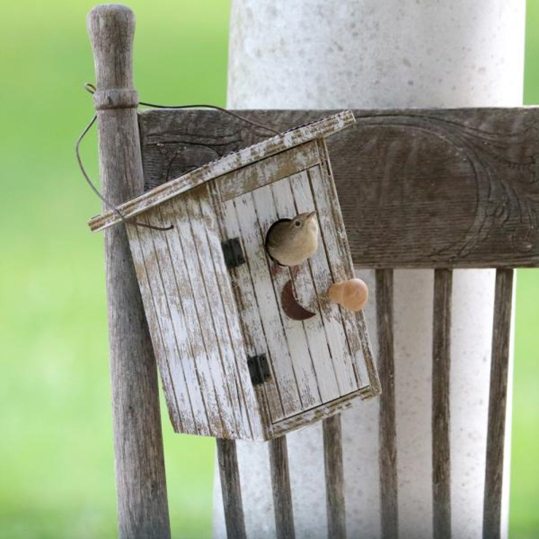 Wooden birdhouse with a bird perched on a rustic wooden post against a blurred green background